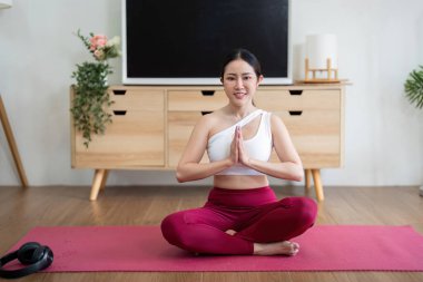Huzurlu bir ortamda, bir kadın geleneksel yoga pozisyonunda oturur, sakinliğini ve farkındalığını vurgular, çalışmasıyla derin bir bağ kurar..