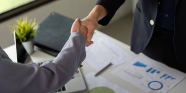 İki iş adamı el sıkışır, anlaşma ve işbirliğini sembolize eder, başarıyı temsil eden grafik ve çizelgeler zeminine karşı koyarlar..