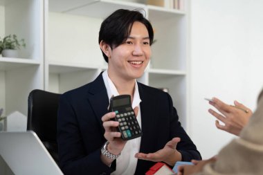 Dost canlısı bir emlakçı, emlak yatırımları hakkında bir konuşma yapar. Finansal yönleri netleştirmek için hesap makinesi kullanır..