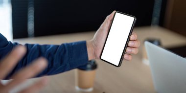 Bir profesyonel, toplantı sırasında modern iş uygulamalarında teknolojinin önemini vurgulayan, bağlantı ve iletişimi sembolize eden bir akıllı telefonu elinde tutuyor..