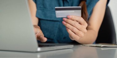 Yakın plan çekimde, dijital finansmanın günlük işlemlerdeki önemini vurgulayarak, online ödemeleri dizüstü bilgisayarla yapmak için kredi kartı kullanan bir kişi görülüyor..
