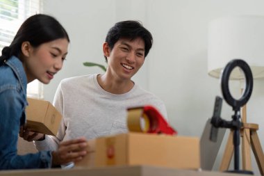 Gülümseyen genç bir adam ve kadın, seyircileriyle canlı yayında iletişim kurarak, girişimci yolculuklarını sergilerken keyifli bir şekilde boks yapan ürünlerdir..