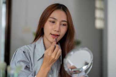 Yansımasına odaklanan bir kadın, güzellik rutini sırasında dudaklarını rujla güçlendirir, canlı renkler sergiler ve kendini ifade eder..