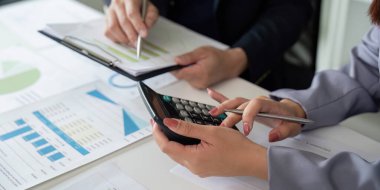 İki profesyonel birlikte veri analiz eder, biri hesaplama yapmak için hesap makinesi kullanır, mali analizde takım çalışması gösterir ve raporlar.