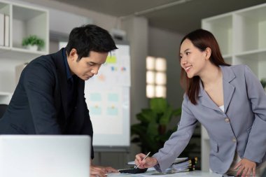Odaklanmış bir iş toplantısı, iki profesyonelin belgeleri gözden geçirmesi ve modern bir ofis alanında birlikte karar vermeleri şeklinde gerçekleşir..