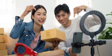 Mutlu çift, izleyicileri için bir video çekerken bir paket tutuyor. Yaratıcı iş girişimlerinde birlikte çalıştıklarında ürünlerine duydukları heyecanı vurguluyorlar..