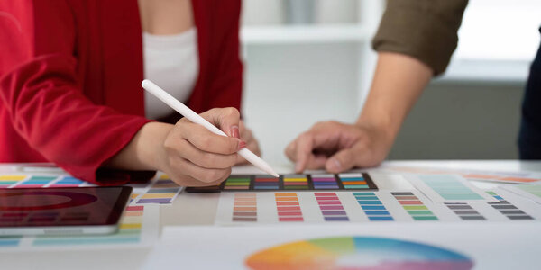 Two designers are engaged in a vibrant discussion about color choices as one utilizes a tablet to complement printed color palettes, showcasing teamwork in digital design.