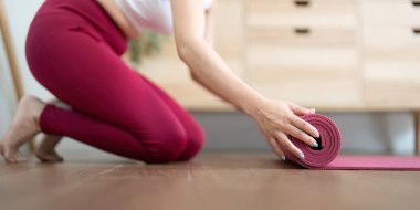 Bir kadın yoga çalışmasını minderini kıvırarak tamamlar. Bu, dikkatli ve içe dönük bir seansın sonunu simgeler..