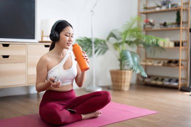 Verimli bir yoga seansından sonra, bir kadın su şişesiyle su içer, sağlığın ve kendine bakmanın önemini vurgular..