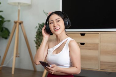 Kulaklıklı bir kadın müzik dinlerken gülümsüyor, rahatlama ve yaşam alanından zevk alarak rahatlığı somutlaştırıyor..