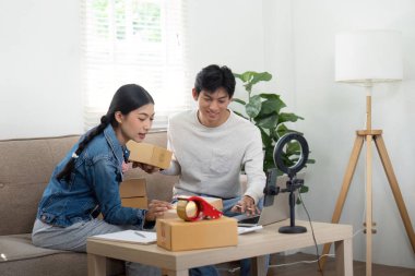 Çift, ana ofislerinde iş stratejileri üzerinde işbirliği yapıyor, fikirleri paylaşıyor ve paketlenmiş kutularla çevrili olarak son ürün sevkiyatlarını inceliyor..