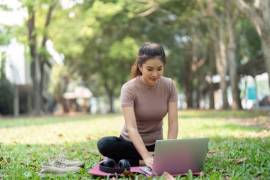 Yoga minderinde oturan bir kadın olarak modern bir iş hayatı dengesi tasviri. Laptopunu doğada kullanıyor, üretkenlik ve sağlığını yaşam tarzında harmanlıyor..