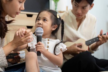 Küçük bir kız çocuğu mikrofona şarkı söylerken neşeli bir etkileşim. Bu arada annesi onu evdeki bir müzik seansında cesaretlendiriyor..