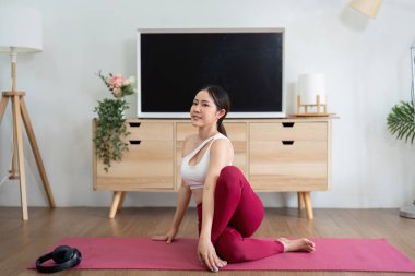 Yoga rutiniyle meşgul olan bir kadın, huzurlu bir yuva ortamında, esneklik ve dengeyi vurgulayarak belirli bir duruş sergiliyor..