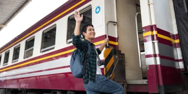 Yüzünde bir gülümsemeyle genç bir adam macerasına başlamak için bir trene biner. Sırt çantası ve kamerası seyahat ve keşif hevesini yansıtıyor..