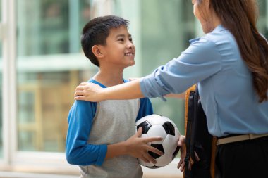 Okul ortamında sıcak bir etkileşim gerçekleşir. Bir anne okuldan sonra oğlunu neşeyle kucaklar ve başarılarını elinde bir futbol topuyla kutlar..