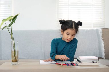 Derinden odaklanmış genç bir kız, canlı renkli kalemlerle çiziyor, yaratıcılığını rahat bir ev ortamında keşfediyor. Bu resim çocukluk hayal gücünü vurgular.