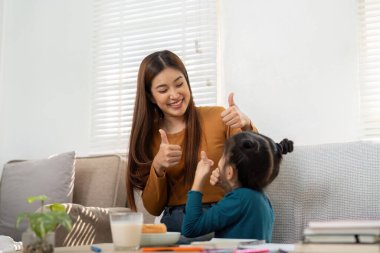 Bir anne ve kızı eğlenceli bir anı paylaşıyor, başparmaklarını uzatıyorlar, birlikte öğrenmenin ve başarmanın sevincini kutluyorlar..