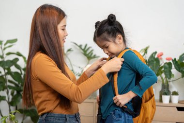 Kendini işine adamış bir anne, kızının sırt çantasını takmasına yardım eder. Önümüzdeki okul gününe hazır ve hazır olmasını sağlar. Bakım ve destek ruhunu somutlaştırır..