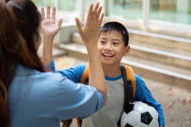 Genç bir çocuk öğretmeniyle takılıyor, okulla ilgili heyecanını sergiliyor. Bir futbol topu tutarak, yeni okul yılına olan heyecanını ifade ediyor..