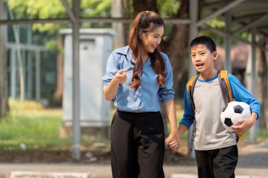 Bir annenin okuldan dönüşünü kutlamak için futbol topu olan oğluyla el ele yürüdüğü neşeli bir sahne..