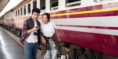 Bir tren istasyonunda, bir çift yan yana durur, bir telefonda seyahat detaylarını kontrol eder, maceraya atılmanın heyecanını gözler önüne serer.