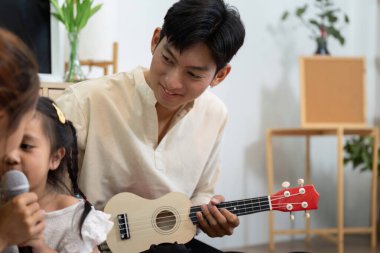 Gururlu bir baba, genç kızı mikrofona şarkı söylerken dikkatle dinler. Aile müzik aktiviteleriyle oluşan bağı vurgular..