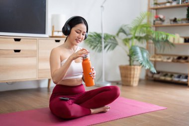 Bir kadın, evdeki yoga seansında enerjisini koruyabilmek için turuncu bir şişeyle su içmek için zaman harcar..