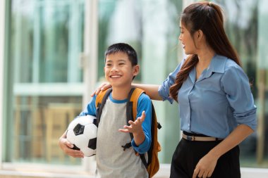 Gülümseyen bir çocuk, dersten sonra düşüncelerini öğretmeniyle paylaşır. Gelecek okul ve futbol aktiviteleri için heyecanlanır..