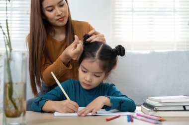 Besleyici bir ebeveyn, kızlarının saçını ev ödevlerine yoğunlaşırken şekillendirir ve günlük hayattaki bakım ile eğitim arasındaki dengeyi belirler..