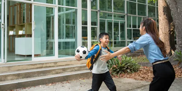 Heyecanlı bir çocuk kolları açık bekleyen annesine doğru koşuyor, okuldan dönüşünü kutluyor, elinde bir futbol topu tutuyor..