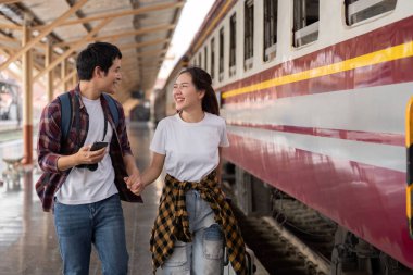 Tren istasyonunda el ele yürürken, bir çift, yaklaşan yolculukları için sevgi ve heyecanı somutlaştıran kahkahaları paylaşıyor..