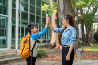 Bir anne ve oğlu bir başka okul gününün başlangıcını kutlayarak beşlik çakıyor. Bu görüntü neşe, cesaret ve aile desteğinin eğitimde önemini temsil eder..