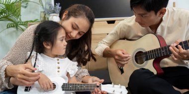 Sıcak bir oturma odasında, bir anne kızına gitar çalmayı sevgiyle öğretir. Etkileşimleri, aile bağlarının ve müzikal öğrenmenin keyfini vurgular..