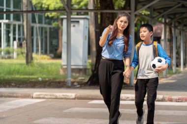 Bir annenin oğlunun elini tuttuğu mutlu bir an. Hem okul günü için heyecanlı, hem de yanında bir futbol topuyla..