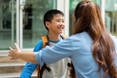 Uzun bir okul gününden sonra, sırt çantalı genç bir çocuk sevinçle annesine yaklaşır, birlikte eve dönmenin heyecanıyla.