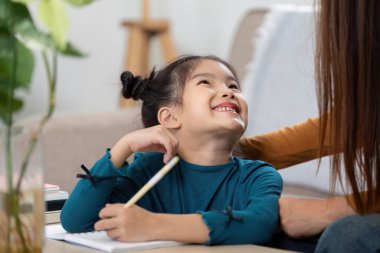 Neşeli bir kız öğrenim seansı sırasında annesiyle konuşurken gülümsüyor. Eğitimin ve kaynaşmanın sevincini gösteriyor..