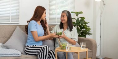 Anne ve kızı bir kase salatayı paylaşıyor. Sağlıklı beslenmenin ve paylaştıkları güçlü bağın keyfini çıkarıyorlar. Evdeki refahı vurguluyorlar..