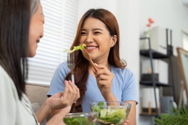 Anne ve kız birlikte gülüyor, salatanın bir ısırığını paylaşıyor, güçlü bağlarını güçlendiriyor ve sağlıklı bir yaşam tarzını destekliyor..