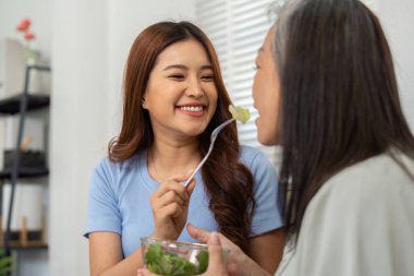 Kızının annesine bir parça salata sunduğu neşeli bir an. Sağlıklı beslenmeye odaklanırken ilişkilerinin eğlenceli ve besleyici yönlerini vurguluyor..