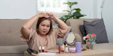 Kadın saçını geriye doğru çekerken, çeşitli ürünler kullanarak güzellik rutinine odaklanıyor, genel görünümünde saç şekillendirmenin önemini vurguluyor..