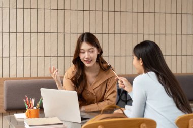 Açık bir çalışma alanında, iki arkadaş öğrenme deneyimlerini geliştirmek için modern teknolojiden faydalanıyor, kahkahaları paylaşırken çeşitli konuları tartışıyorlar..