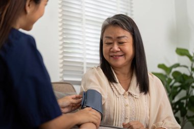 Özenli bir bakıcı yaşlı bir kadının kan basıncını ölçer ve sağlığının özen ve hassasiyetle izlenmesini sağlar..