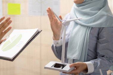 Bir kadın, toplantı sırasında bir model kullanarak sürdürülebilir uygulamaların iş kararları üzerindeki etkisini gösteren rüzgar enerjisinin önemini anlatıyor..