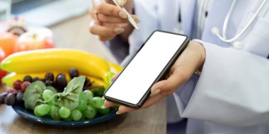 Bir sağlık danışmanlığında, bir doktor beslenme bilgilerini sunmak için teknolojiden faydalanıyor, beslenme planlarına taze meyve eklemenin önemini vurguluyor.