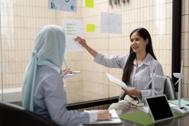 İki profesyonel, sürdürülebilir veri ve yeşil enerji modellerini incelerken, şirketlerinin ESG hedefleri için strateji oluşturan bir toplantıda işbirliği yapmaktadır..
