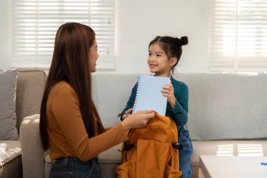 Genç bir kız okul heyecanını gösteren defterini annesine sunar. Bu an öğrenmenin ve ebeveynlerin desteğini yansıtıyor..