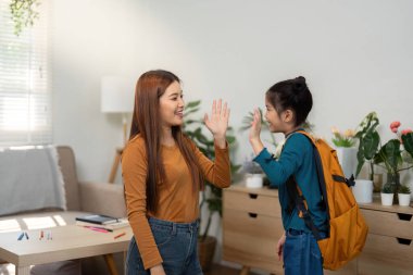 Anne ve kızı sevinçli bir beşlik paylaşıyor, önlerindeki günün heyecanını dile getiriyorlar. Bu an destek ve beraberliği temsil ediyor..