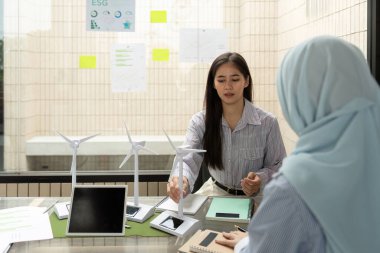 İki profesyonel, ESG stratejileri ve sürdürülebilir enerji çözümleri üzerinde yoğunlaşarak verimli bir toplantıda yer alıyor. Rüzgâr türbini modellerini analiz edip çevresel girişimleri tartışıyorlar..