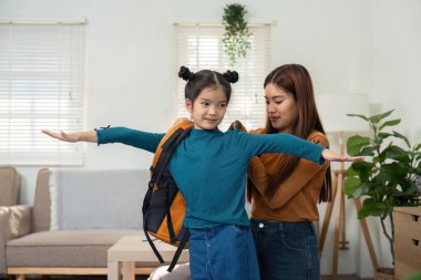 Sevgi dolu bir jest olarak, bir anne kızının sırt çantasını takmasına yardım eder, öğrenme ve eğlenceyle dolu bir güne uygun hale getirilmesini sağlar..